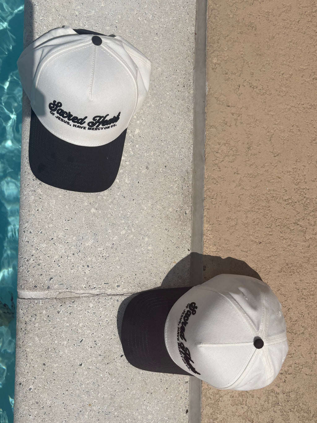 Two hats, one white and one black with text, leaning against a poolside wall.
