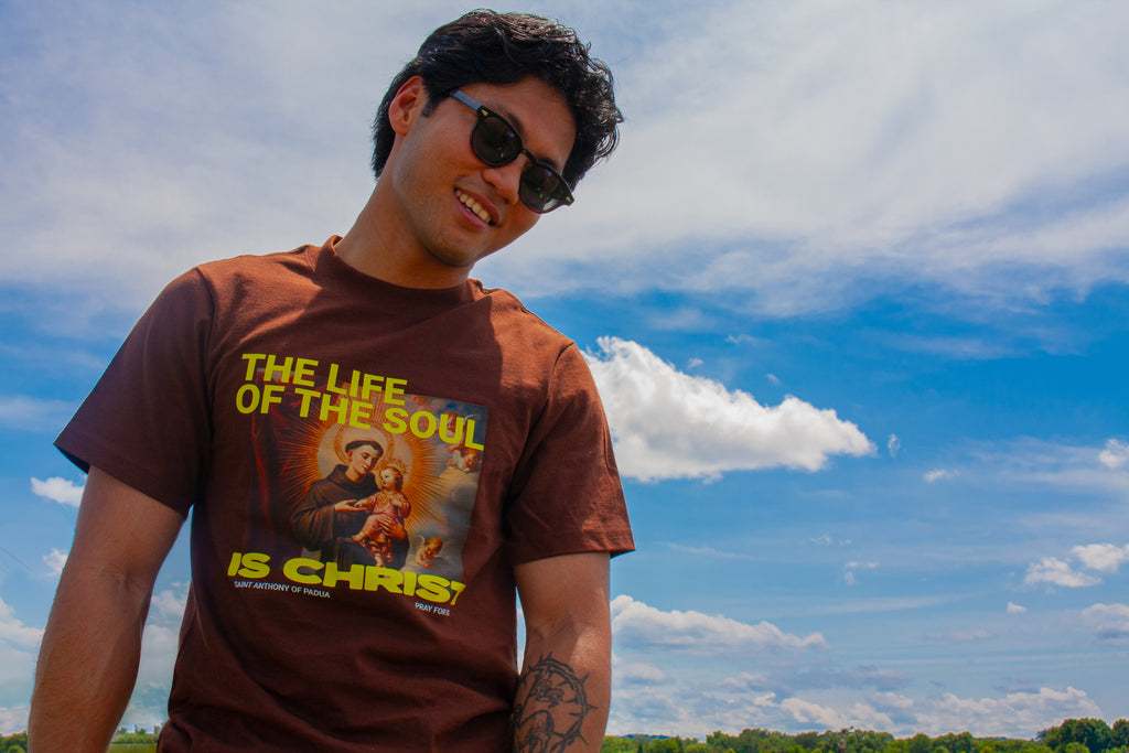 Person wearing a brown t-shirt with a graphic design against a blue sky