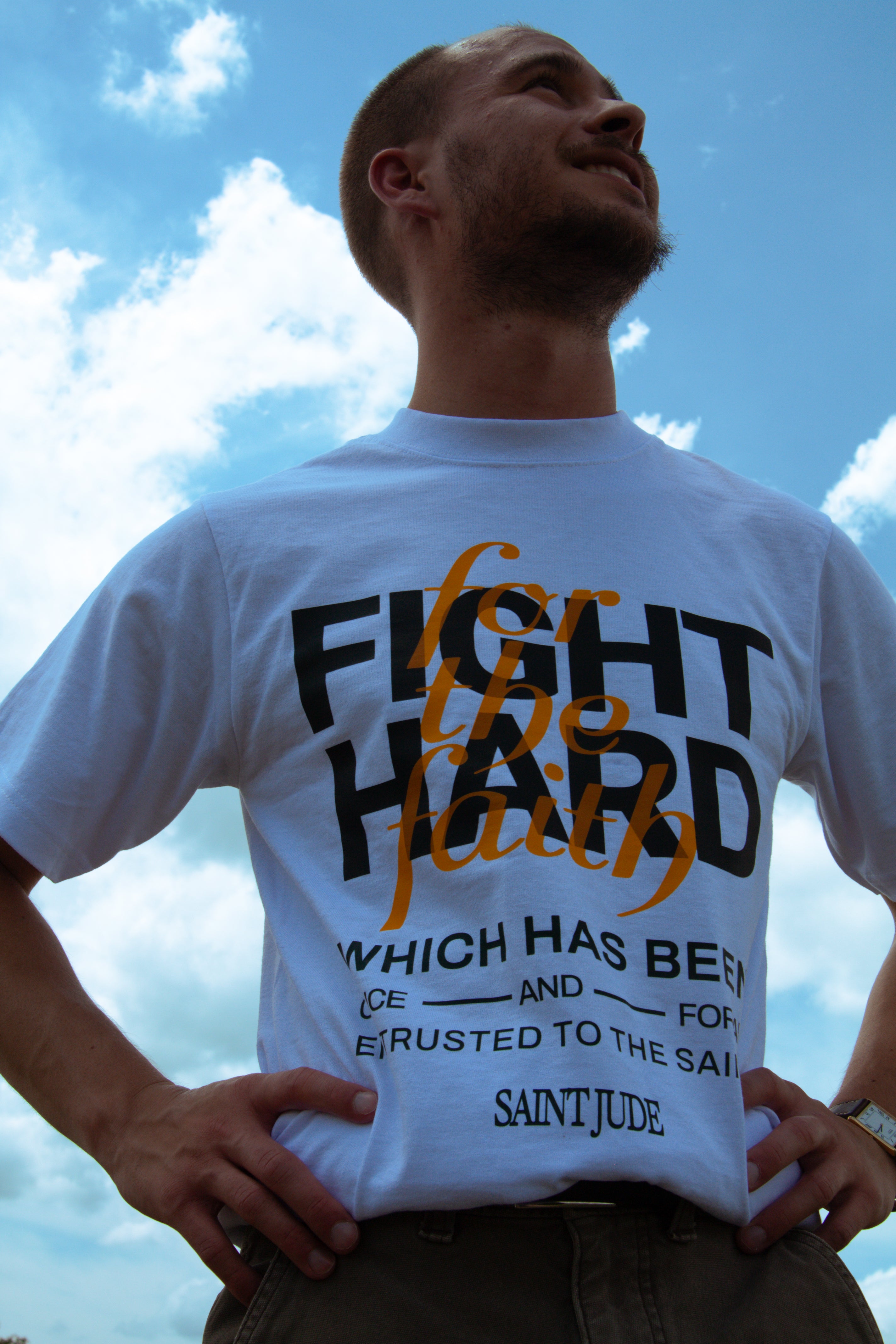 Man wearing a white t-shirt with 'Fight the hard fight which has been prepared for you' text against a blue sky.